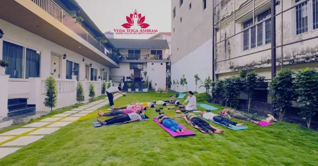 Students practicing guided yoga and meditation on a lush green lawn at the Best Yoga Ashram in Rishikesh during a peaceful morning session.